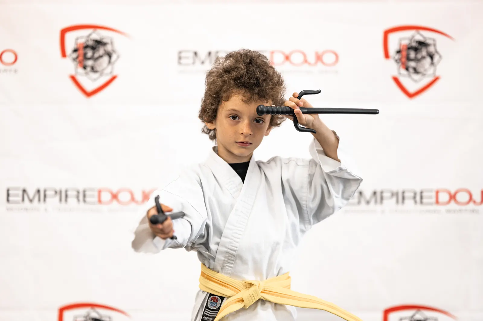 Young Empire Dojo student in a white gi and yellow belt practicing with training sai